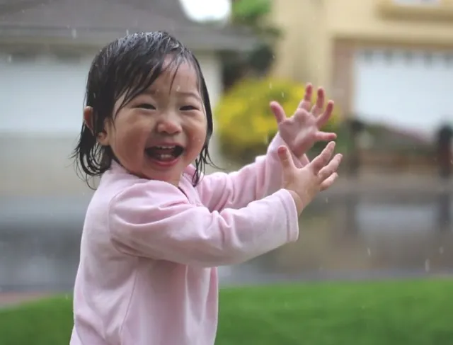 Menina de 15 meses de braços abertos à chuva, no momento em que sente as primeiras gotas
