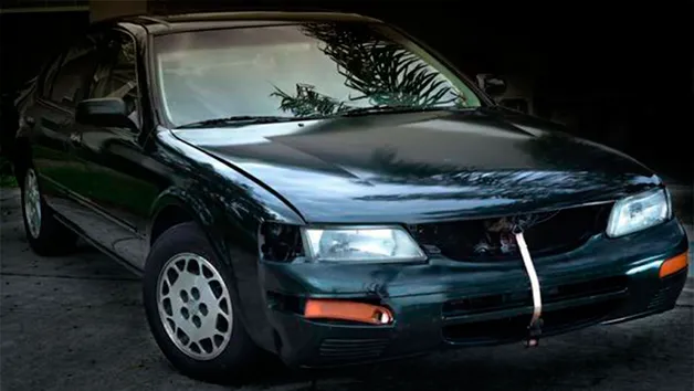 Nissan Maxima de 1996 verde-escuro, com o para-choques da frente preso por uma cinta
