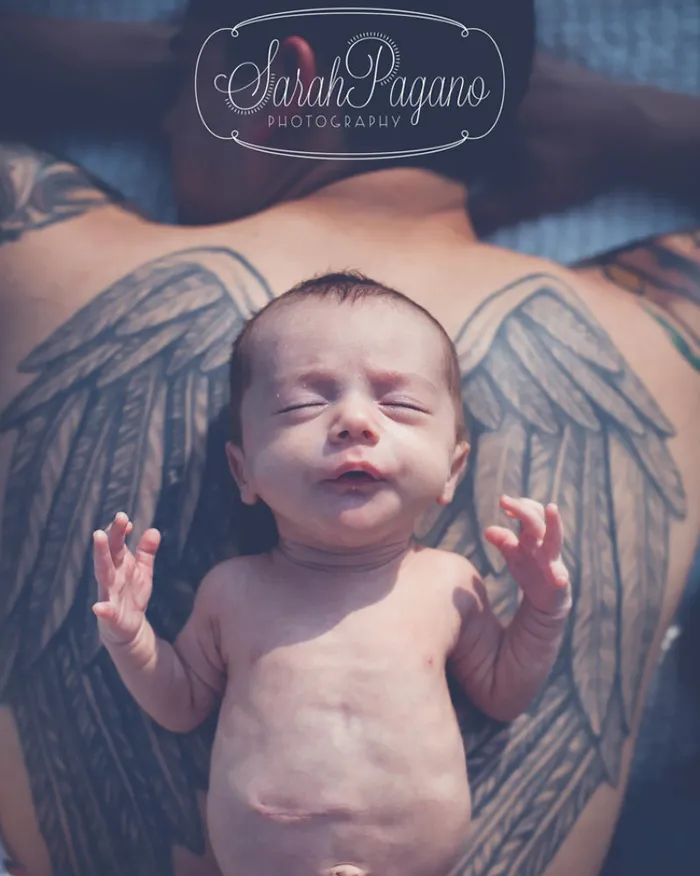 Bebé recém-nascido deitado sobre as costas do pai, que tem um par de asas tatuadas
