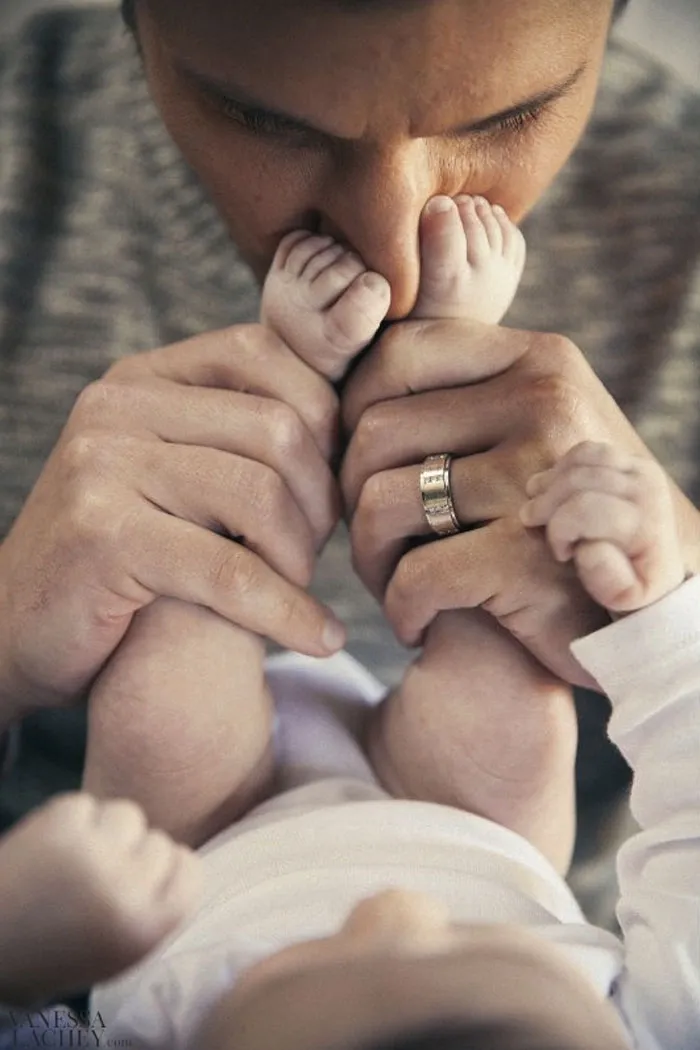 Pai a beijar os pés do bebé, que segura entre as mãos, com aliança no dedo