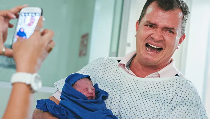 Pai de bata de hospital a chorar de alegria com o recém-nascido embrulhado numa manta azul