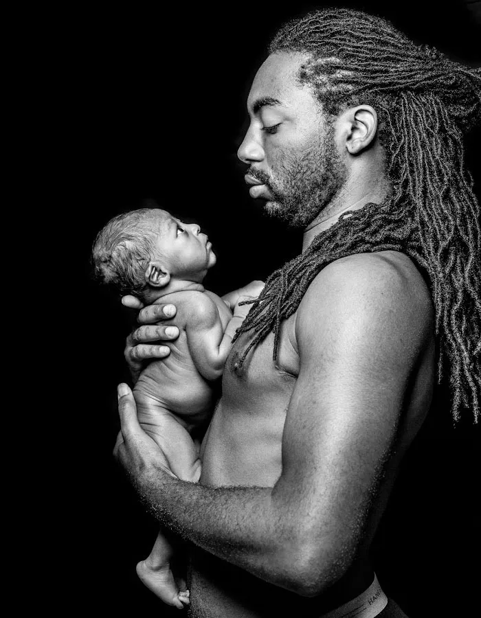 Pai de rastas segura o filho recém-nascido nos braços, numa fotografia a preto e branco