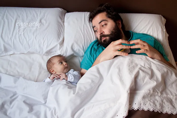 Pai deitado na cama olha de lado para o bebé recém-nascido deitado ao seu lado