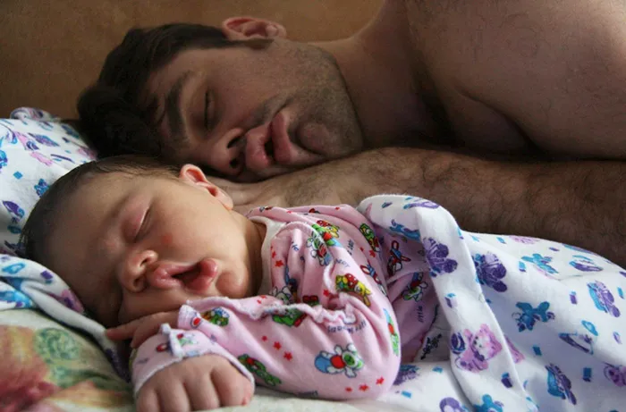 Pai e bebé a dormir encostados um ao outro, o bebé com um pijama estampado com flores