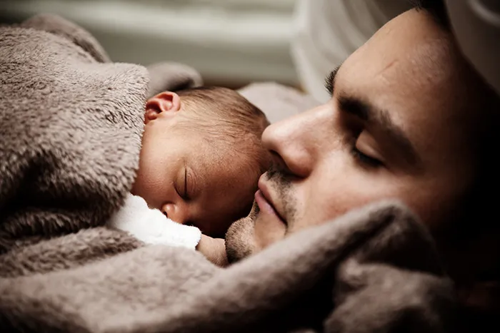 Pai e recém-nascido a dormir encostados, cara com cara, embrulhados numa manta