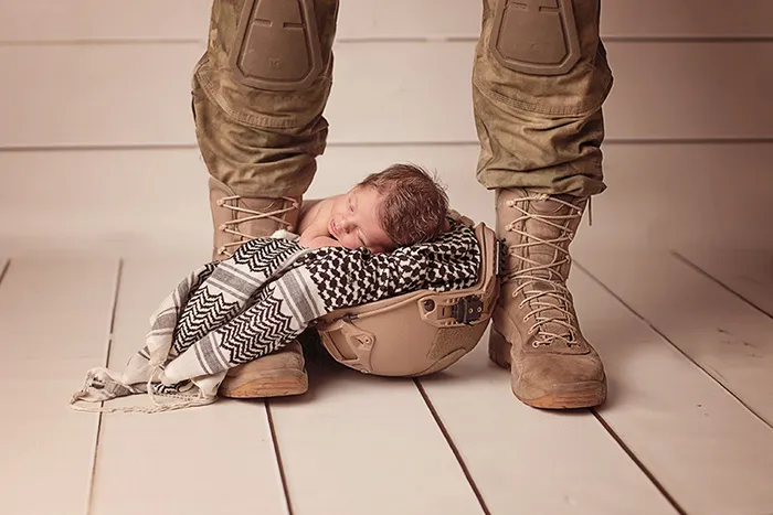 Recém-nascido a dormir num capacete militar entre as botas do pai, que está de pé