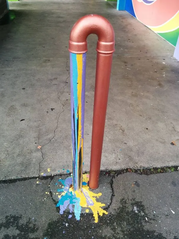 Cano de cobre pintado com tinta de várias cores a escorrer até ao chão