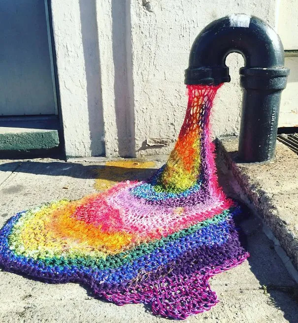 Croché com as cores do arco-íris a sair de um cano de metal e a espalhar-se pelo chão