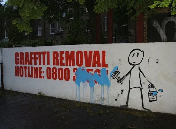 Muro com a frase linha de remoção de graffiti em letras vermelhas e um boneco a pintar por cima do número de telefone