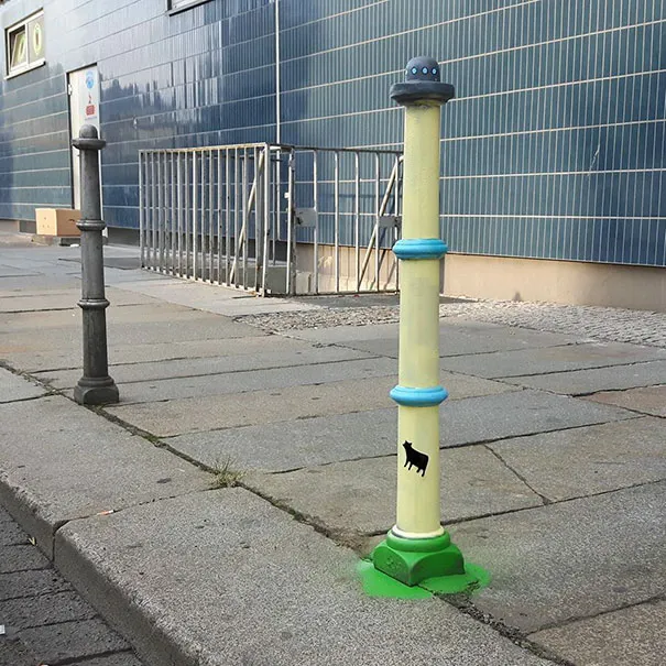 Pilarete de rua pintado como um disco voador verde a raptar uma vaca com um raio de luz