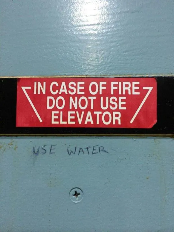 Placa vermelha a dizer em caso de incêndio não use o elevador, com use água escrito à mão por baixo