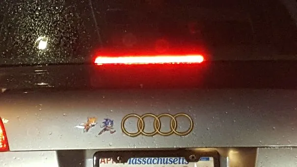 Traseira de um Audi com autocolantes do Sonic e do Tails a correr ao lado dos quatro anéis