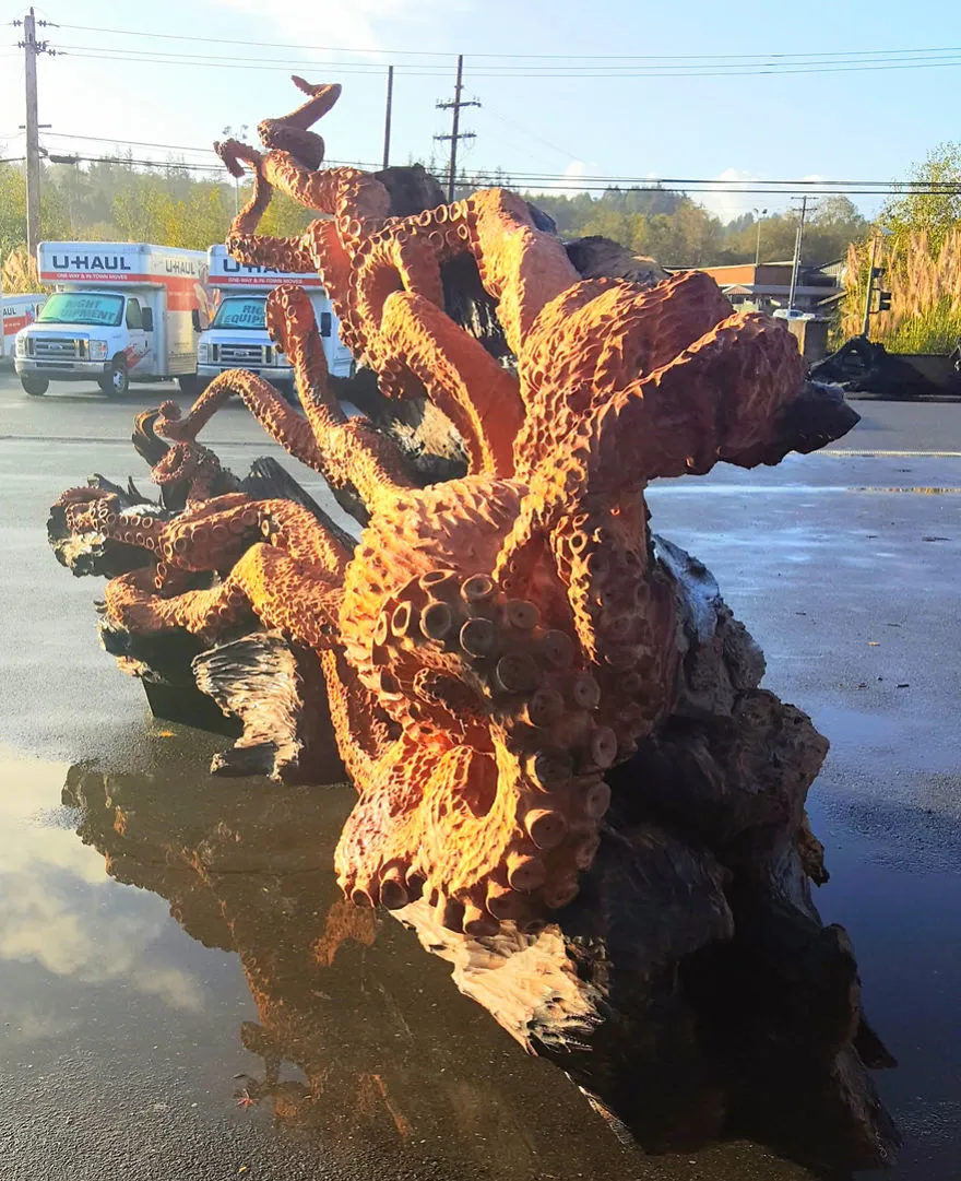 A escultura vista de frente, com a cabeça do polvo e os tentáculos a subir, refletida no chão molhado