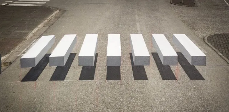 Passadeira pintada em 3D numa rua de Ísafjörður: as riscas brancas parecem blocos levantados com sombra no alcatrão