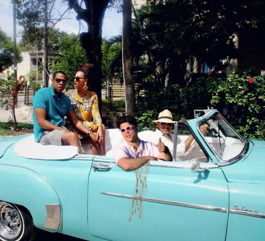Average Rob de óculos escuros num descapotável azul-turquesa com um casal e um homem de chapéu