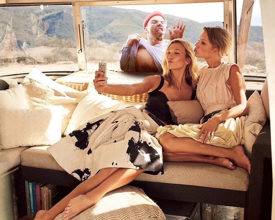 Duas mulheres a tirar uma selfie no sofá de uma autocaravana, com Average Rob espremido atrás delas