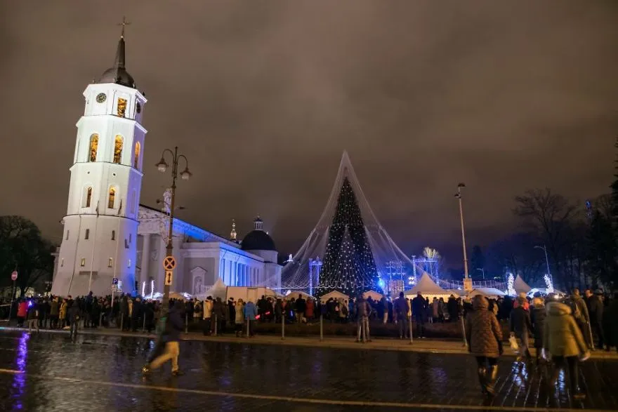 Árvore de Natal ao lado do campanário da Catedral de Vilnius numa noite de chuva, com pessoas na praça