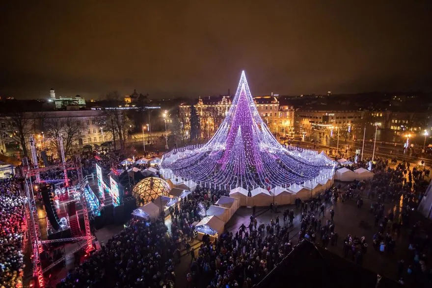Árvore de Natal de Vilnius iluminada, rodeada pela multidão e pelas casinhas do mercado de Natal