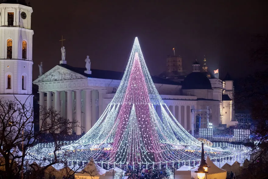 Árvore de Natal em forma de cone com luzes brancas e roxas diante da Catedral de Vilnius