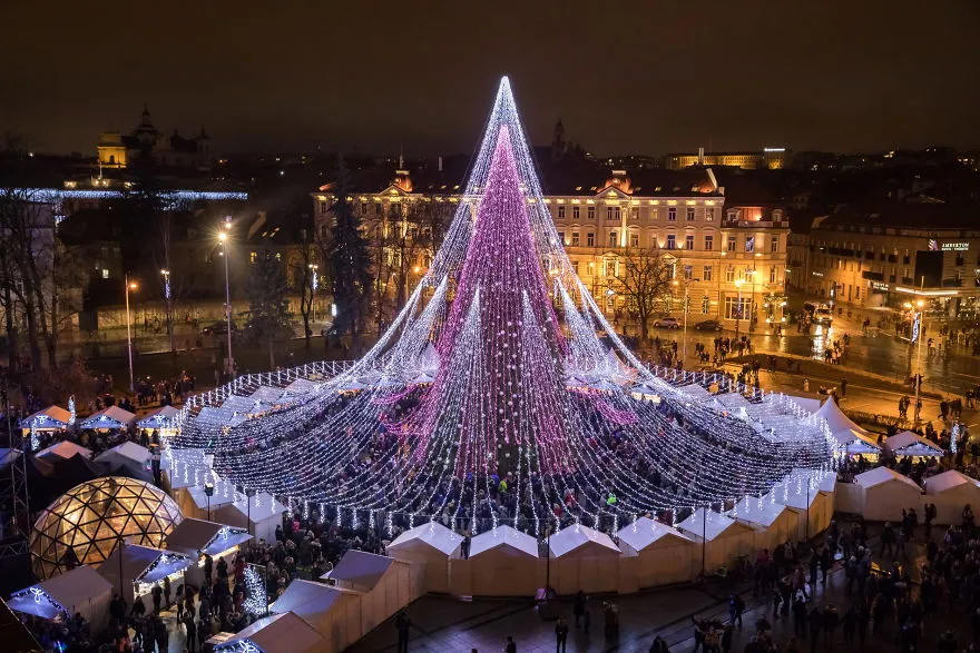 Vista aérea noturna da árvore de Natal de Vilnius em 2017, um cone de luzes brancas e roxas no meio da Praça da Catedral
